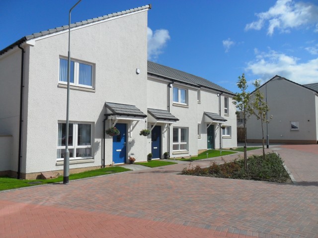 Row of modern new build council houses with blue doors, small front gardens, and a paved walkway. A streetlamp stands nearby under a sunny, partly cloudy sky - Housing First project helping tackle Fife's housing emergency