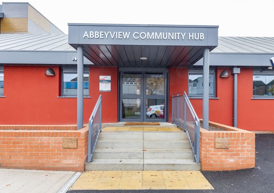Exterior of the entrance to Abbeyview Community Hub, with stairs to the front. Building is red with grey roof and awning.