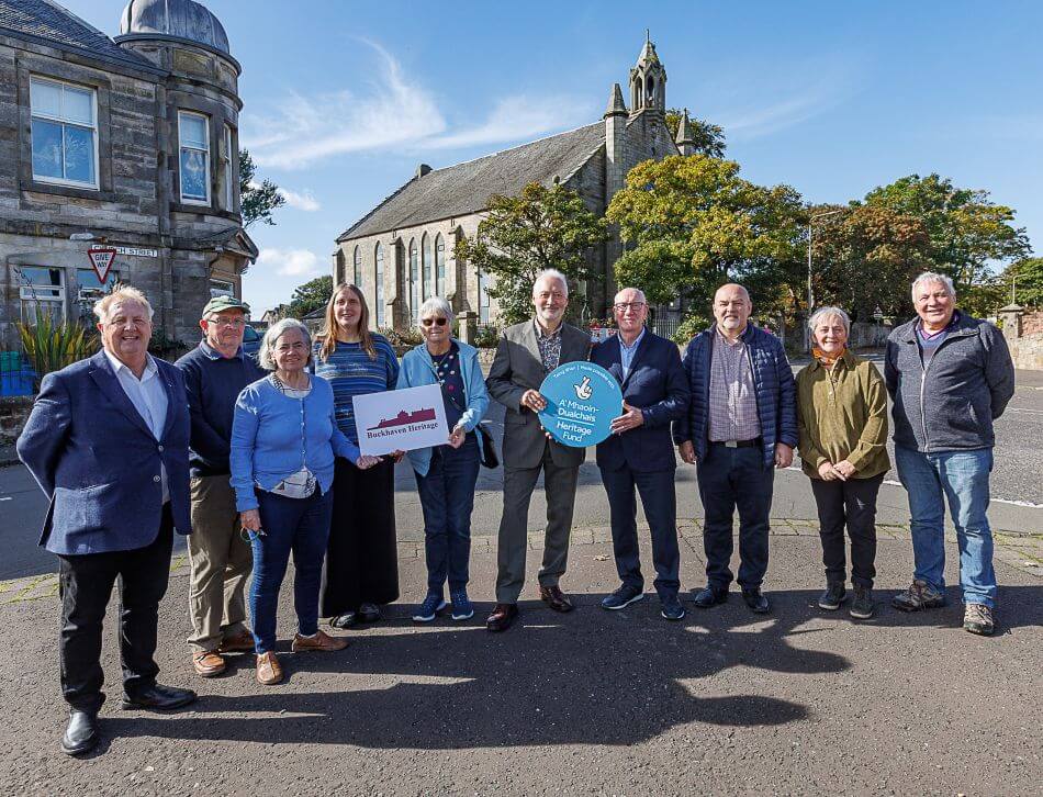 A group of people in front of historic Buckhaven Church holding signs for the National Lottery and Buckhaven Heritage