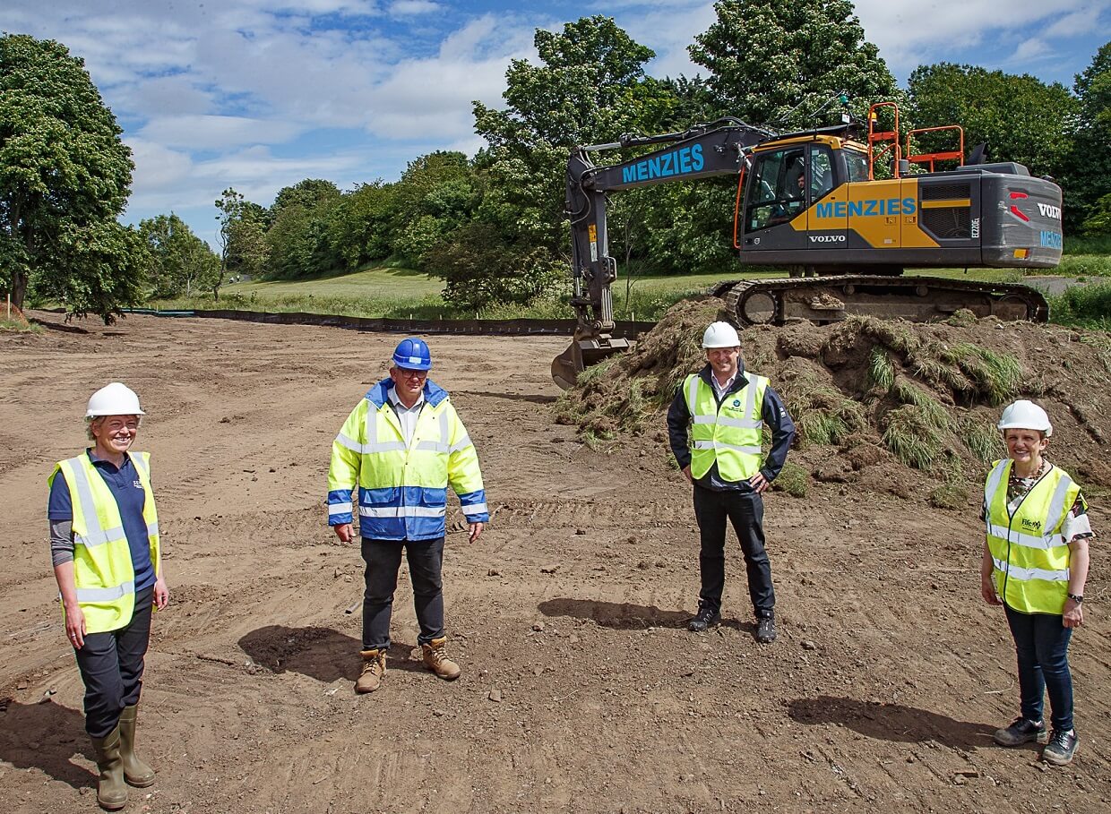 Workers standing on site in front of excavator