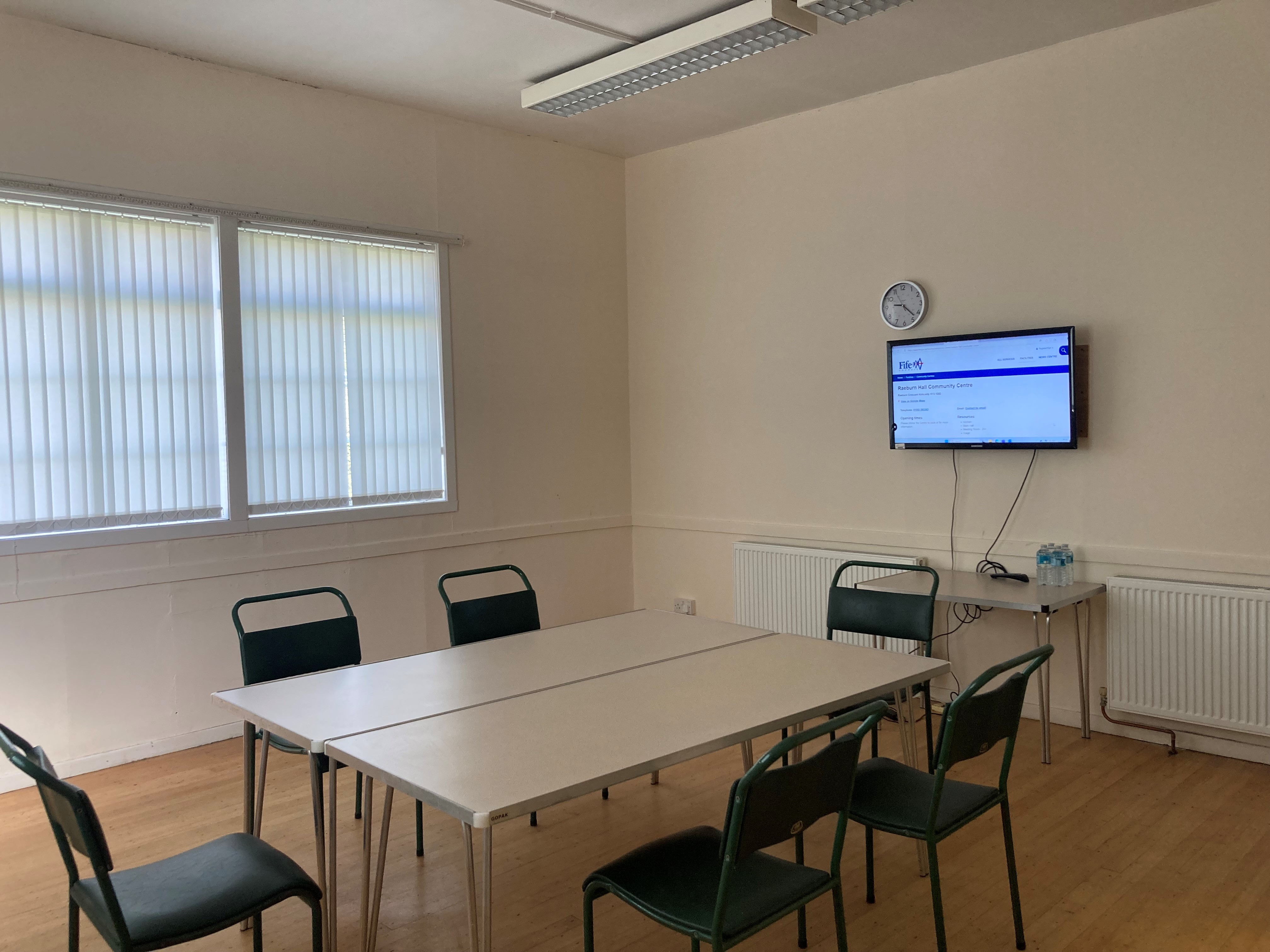 Small meeting room with a table and six chairs. Room has two windows with blinds, a wall-mounted TV, a separate small table, wooden flooring and ceiling lights. Small meeting room with a table and six chairs. Room has two windows with blinds, a wall-mounted TV, a separate small table, wooden flooring and ceiling lights.
