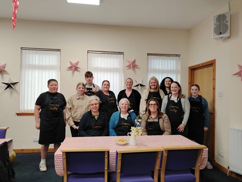 Burntisland Suppers People standing in front of three windows and behind a table