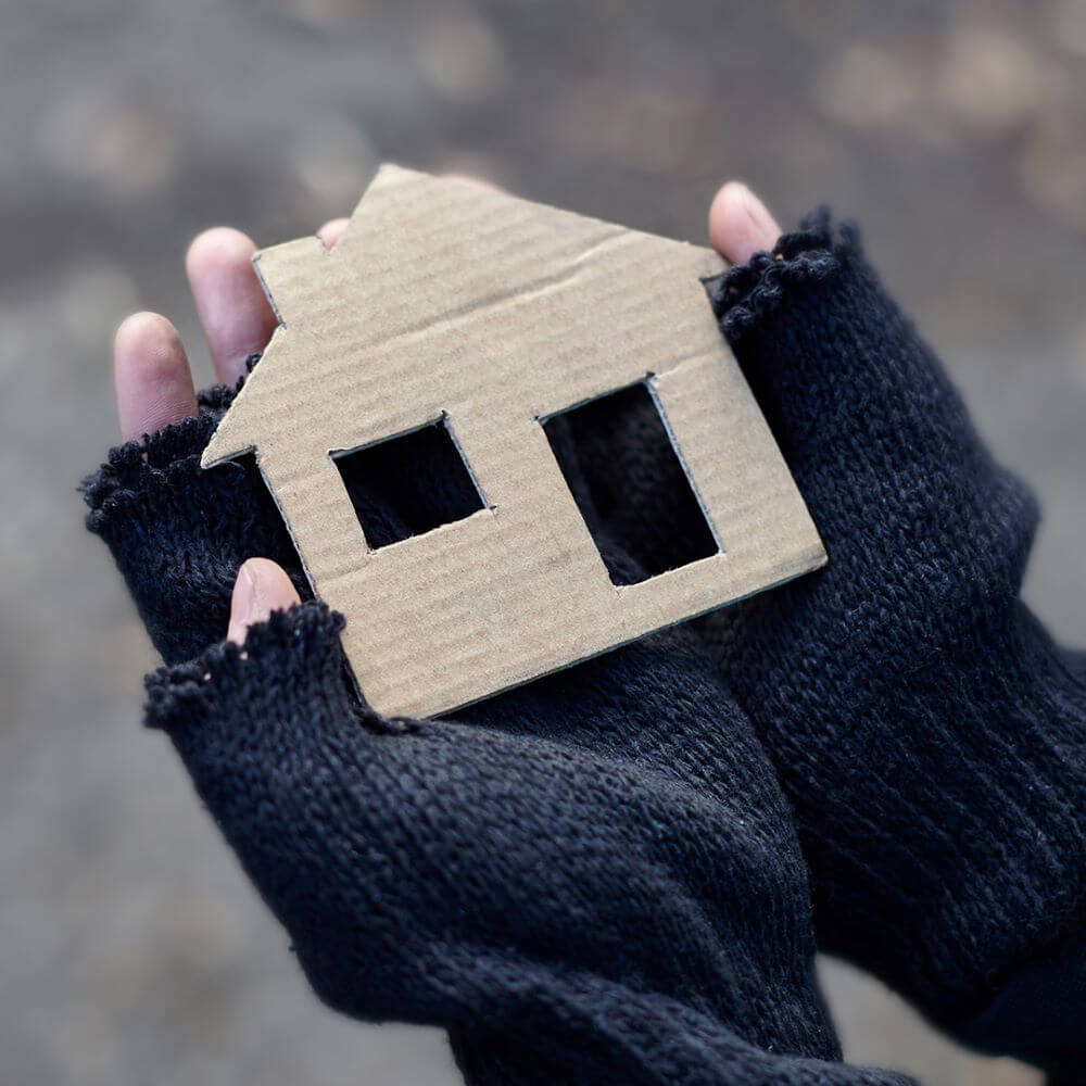 Hands in woollen, fingerless gloves holding a small cardboard cut out of a house - Help us to help rough sleepers