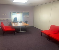 a room with a desk, a computer, and red chairs