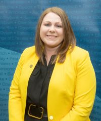 Cllr. Holton wearing yellow in front of blue background