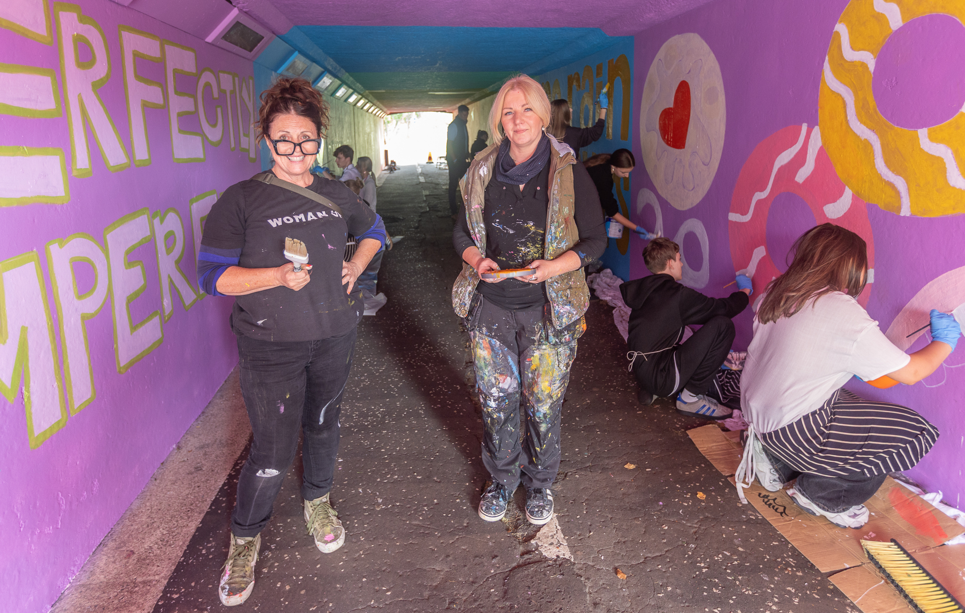 Local artists Vanessa Gibson and Donna Forrester in Auchmuty underpass with a group of young people painting a mural.