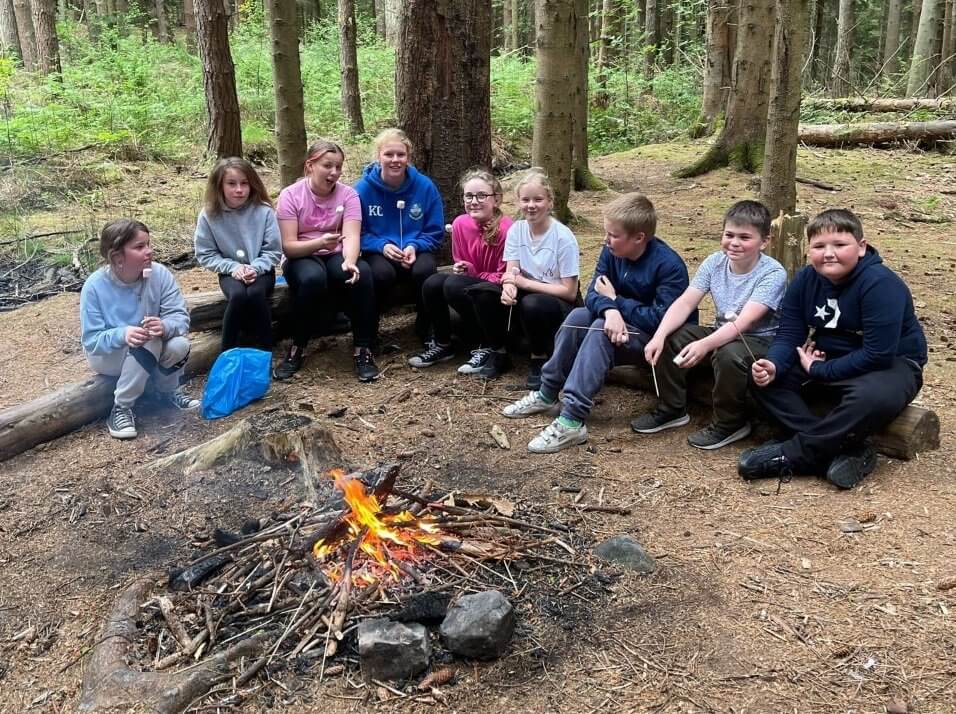nine children and young people sitting around a campfire in the woods