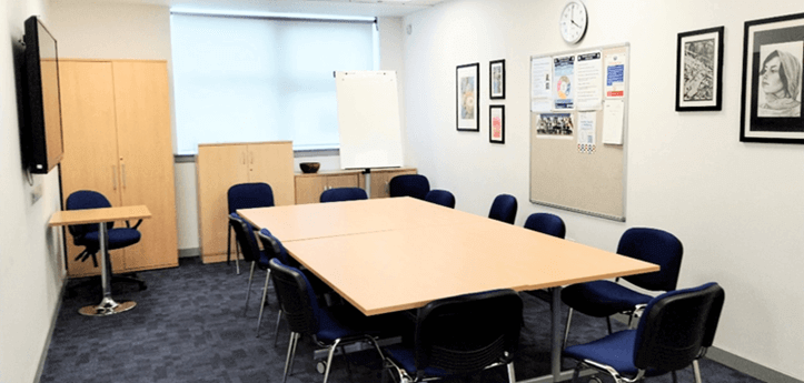 meeting room A meeting room. A large table and chairs fill the center. A whiteboard and TV are nearby.