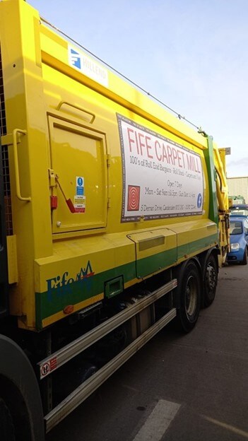 Close up shot of a yellow bin lorry with Fife Carpet Mill advert on the side Close up shot of a yellow bin lorry with Fife Carpet Mill advert on the side