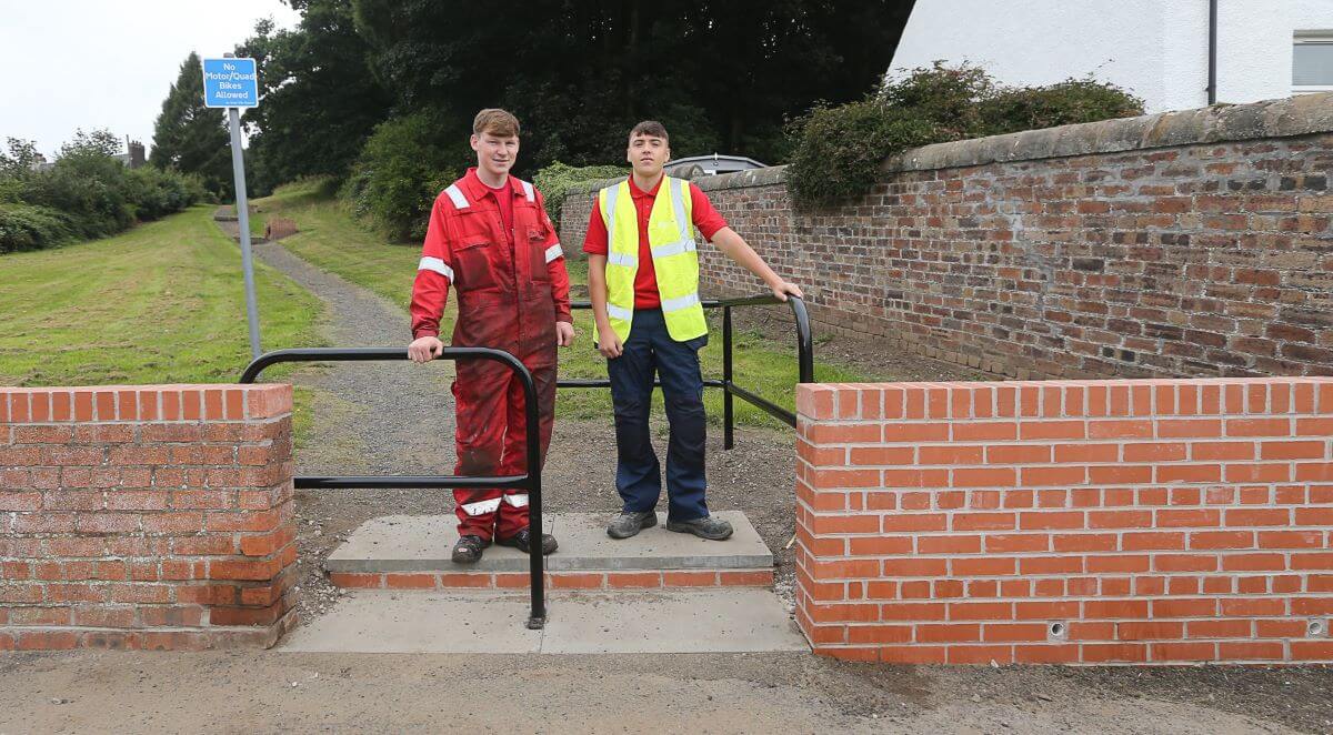Kyle Keddie, apprentice fabricator, and Harvey Ross, apprentice bricklayer stand next to the wall they re-built - Council apprentices seize opportunity to complete re-build of community eyesore