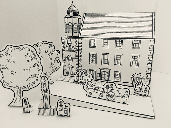 Black‑and‑white paper diorama showing a historic street scene with buildings, trees, people, and a horse‑drawn cart.