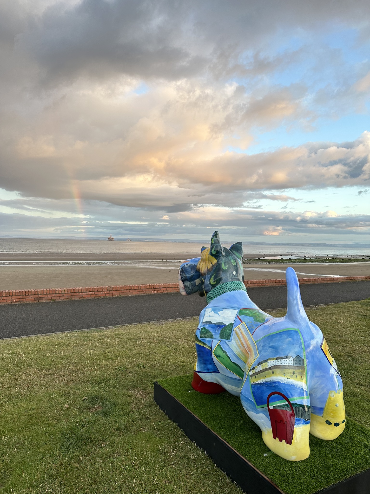 A large, colorful statue of a Scottish Terrier dog overlooking a beach