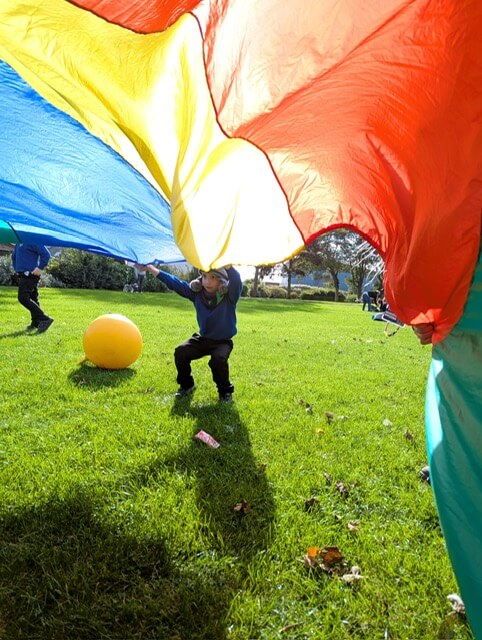 Child holding a colorful parachute outdoors with a large yellow ball on the grass.