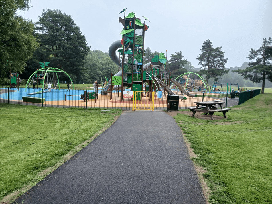 Playground with climbing structures, slides, swings, and a picnic table in a grassy park setting