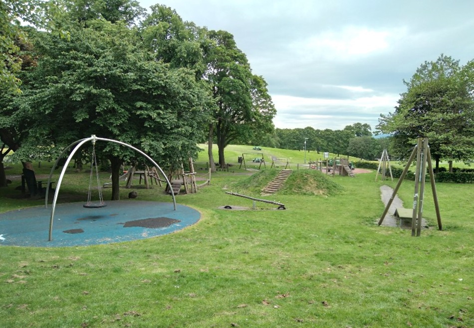 Playground with swings, seesaw, and climbing structures surrounded by grass and treesk