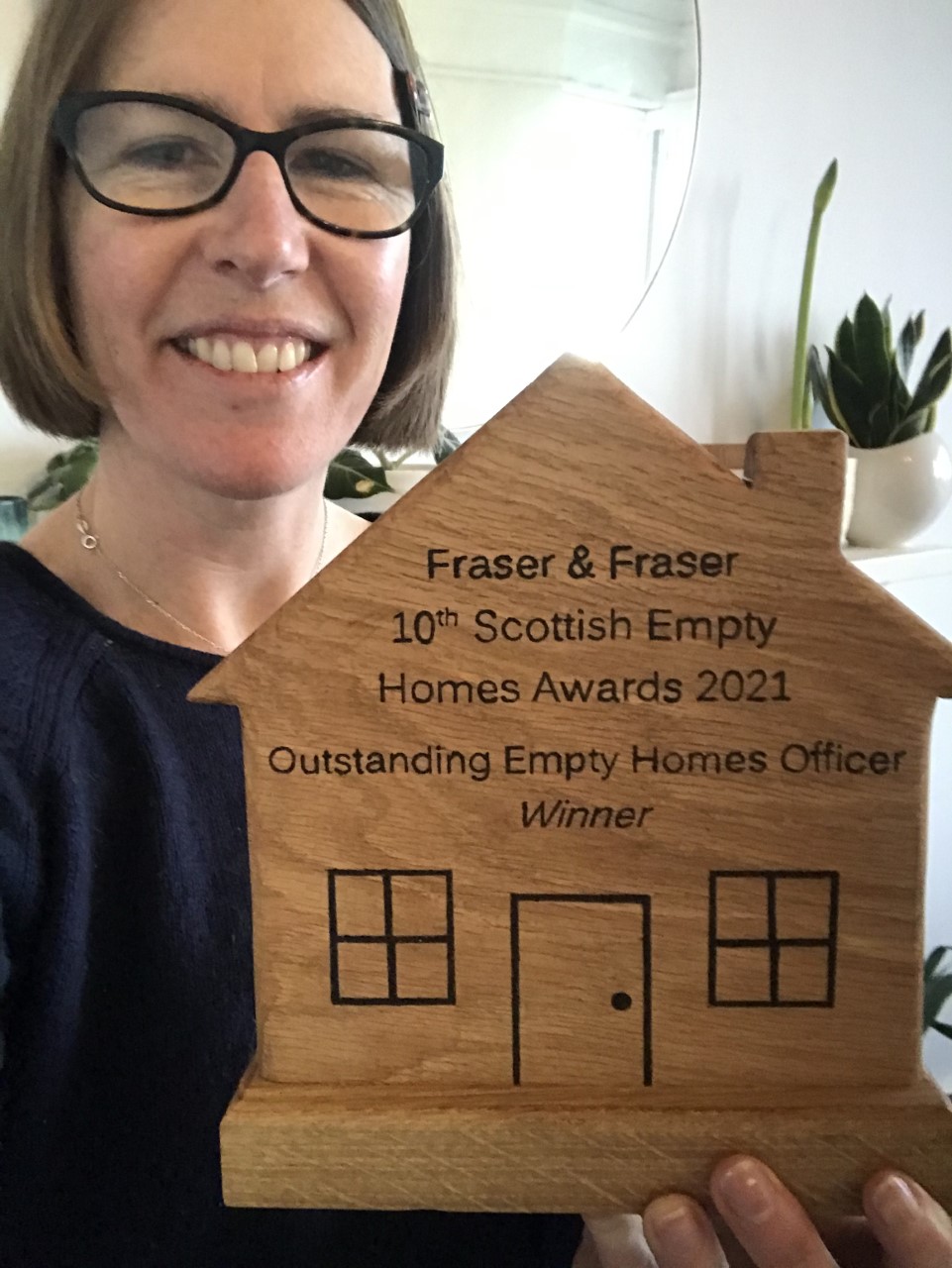 Person holding a wooden house-shaped award engraved with “Scottish Empty Homes Awards 2021 – Outstanding Empty Homes Officer Winner”.