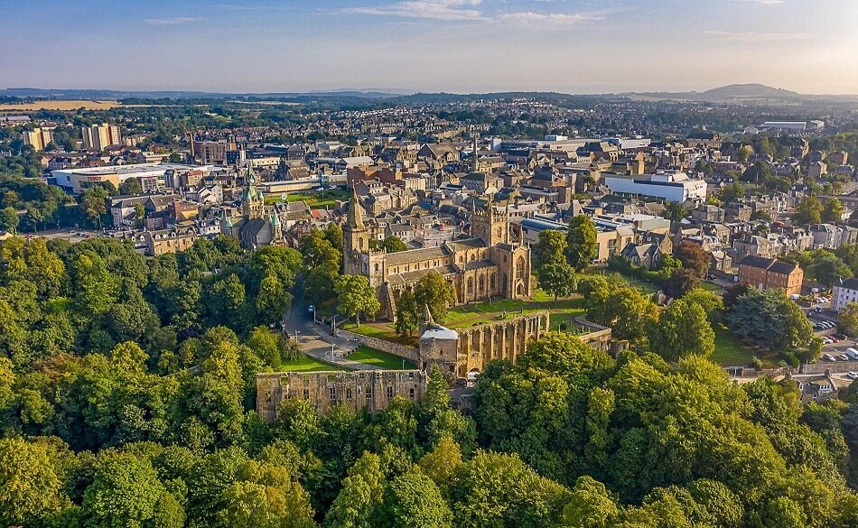 Aerial picture with Dunfermline Abbey surrounded by trees in the foreground. The background shows Dunfermline's urban landscape to the south. 