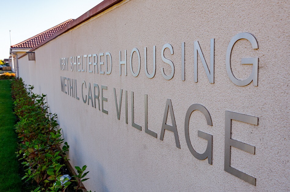 Methil Care Village signage on a communal wall, with gardens and plants to the front