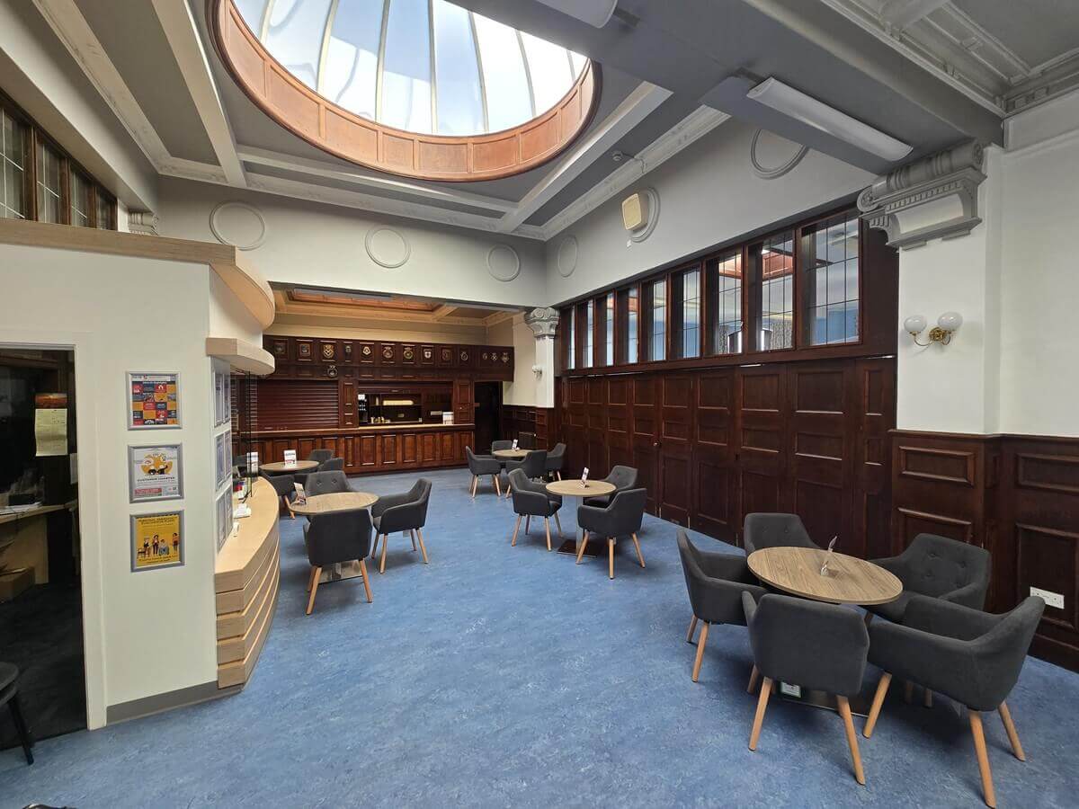 Bright lounge area with round tables and chairs, dark wood panelling, a skylight dome above, and a bar counter at the back