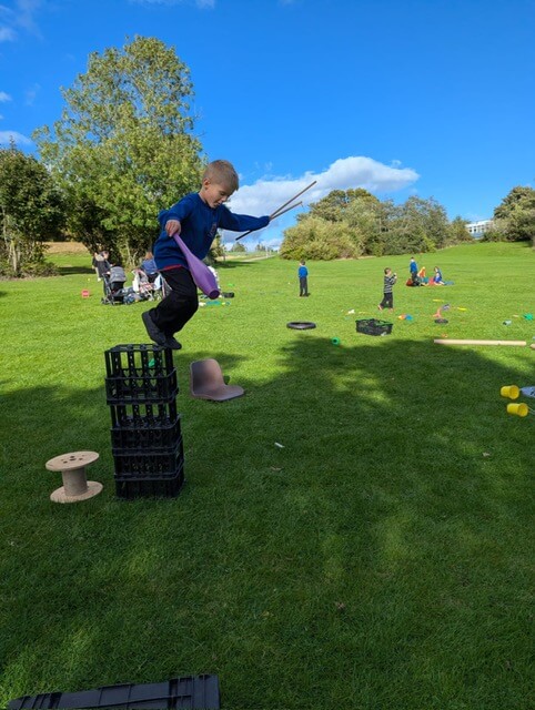 Child balancing on stacked crates holding sticks during outdoor play.