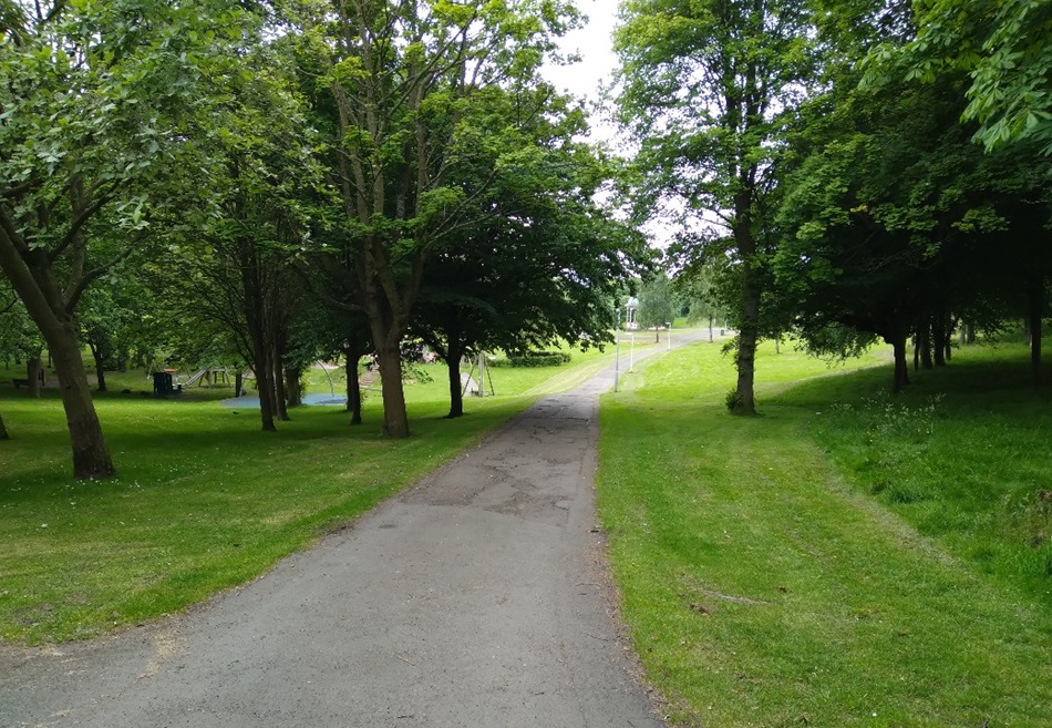 Paved path through a grassy, tree-lined park area