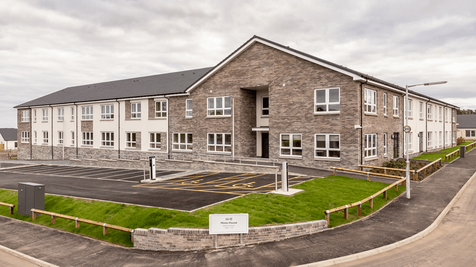 Exterior view of housing scheme at Jenny Gray House, with quiet residential road and green garden to the front. Artist's impression of the housing scheme at Jenny Gray House, with quiet residential road and cyclists on the road.