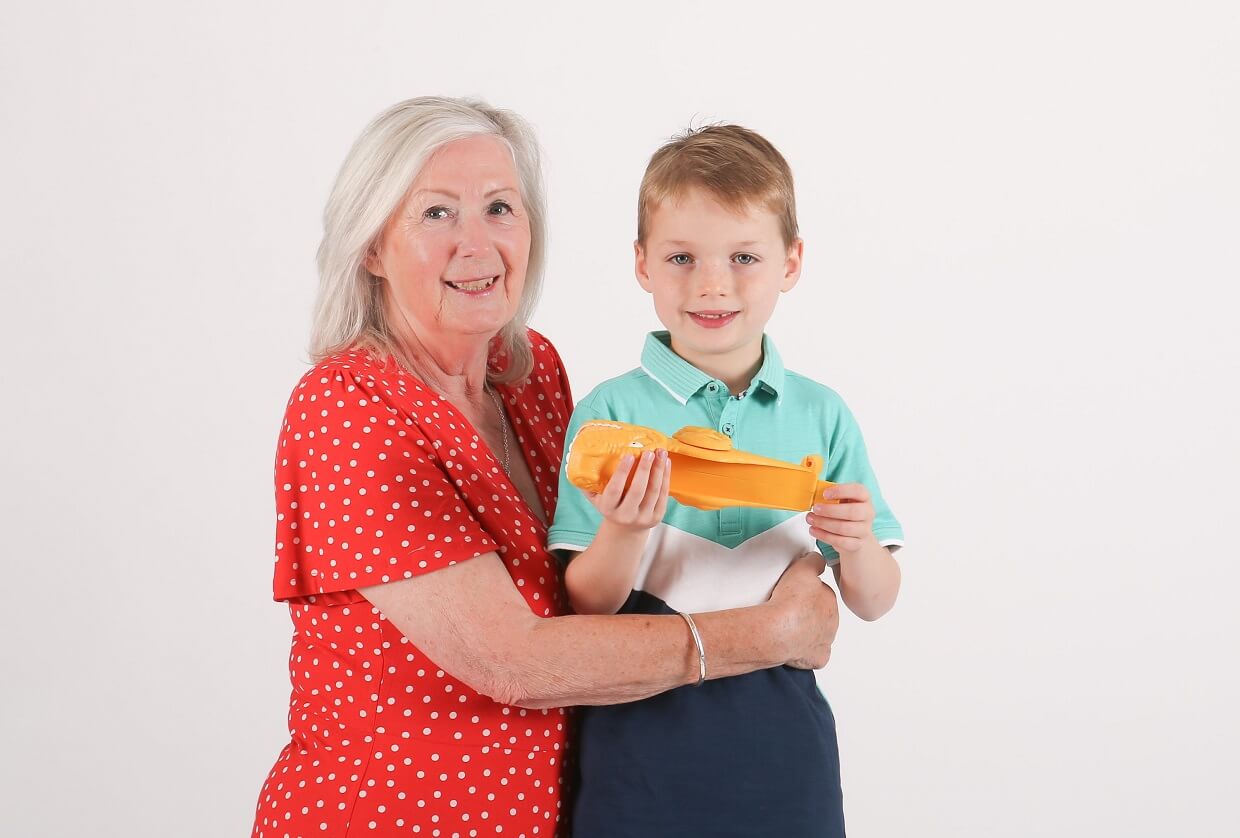 Woman in a red dress kneeling beside a young boy who is holding a toy. The woman's arms are around the boy's waist.