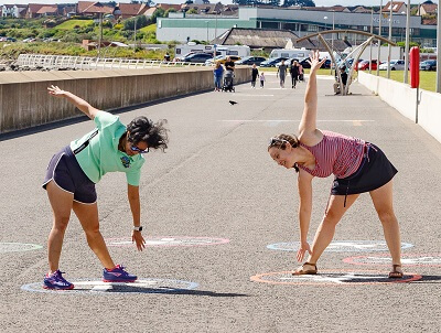 Kirkcaldy waterfront playground games 21 Two ladies stretching - pointing down to the ground and up to the sky