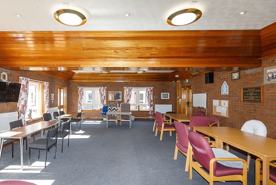 Communal living and dining space with tables and chairs and TV on the wall
