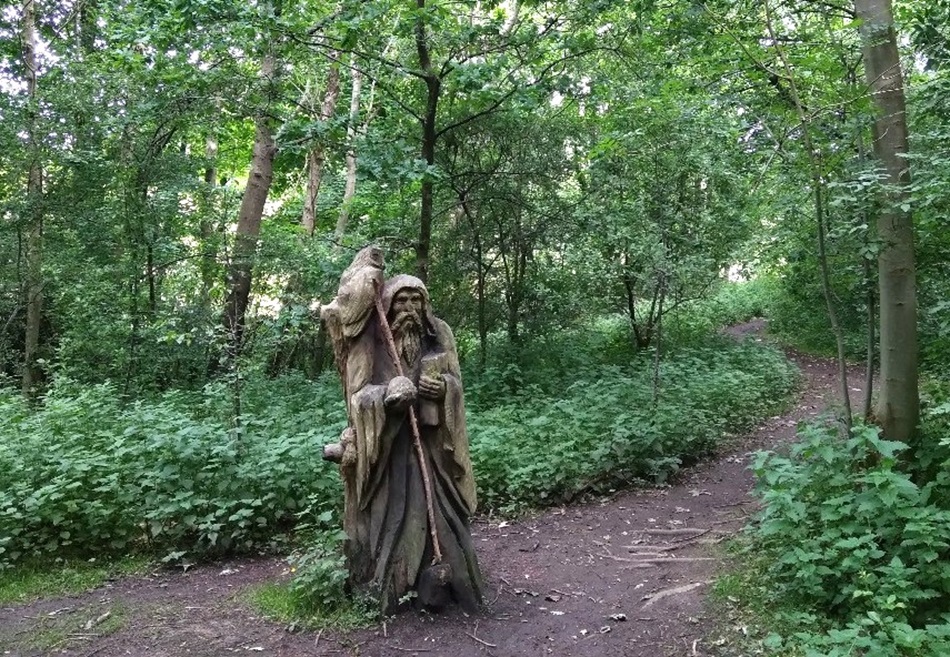 Hooded figure statue within a wooded area and dirt path