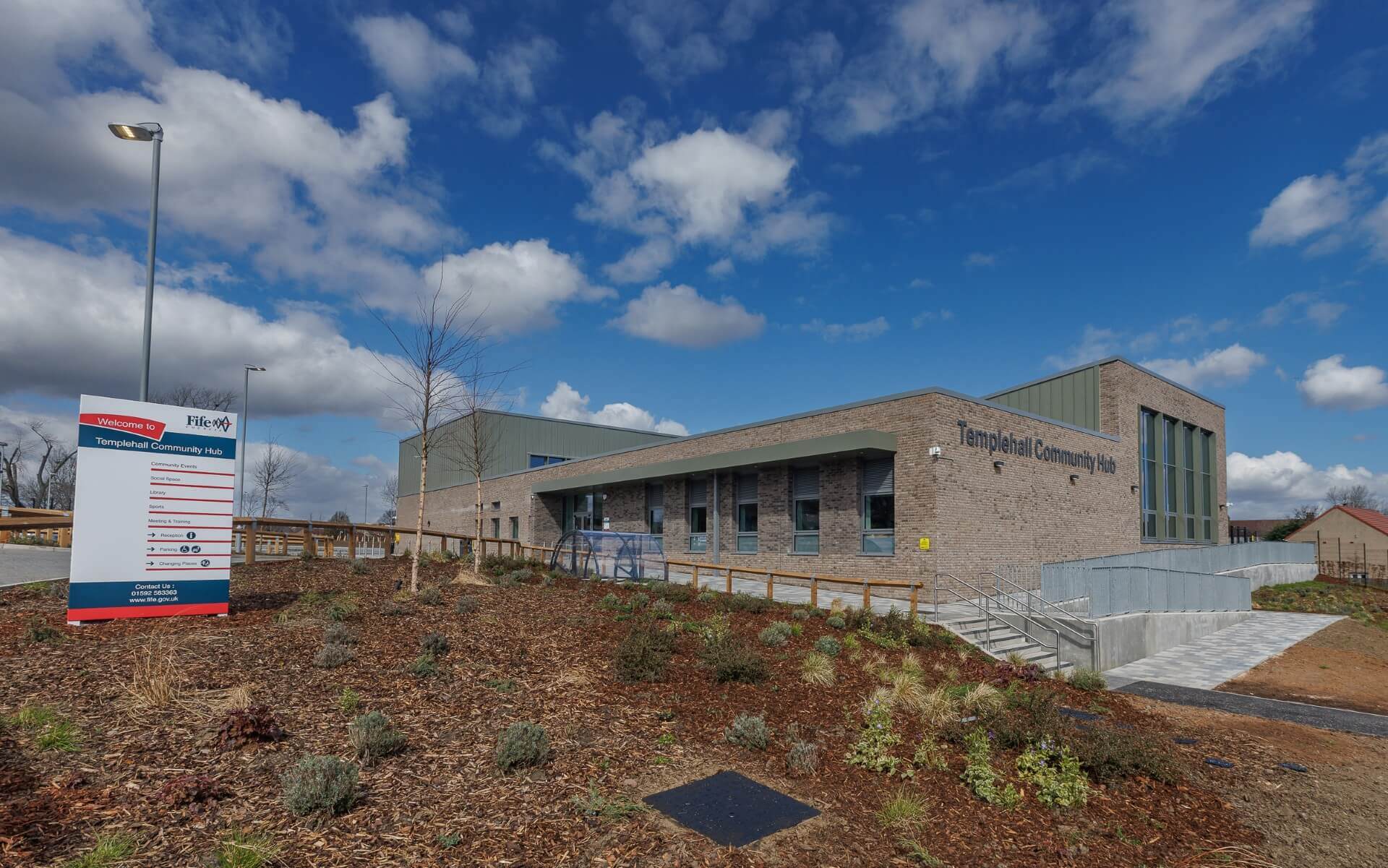 Aerial view of Templehall Community Hub, a modern single‑storey building with a flat roof, light brick walls, and surrounding paved walkways and parking areas.