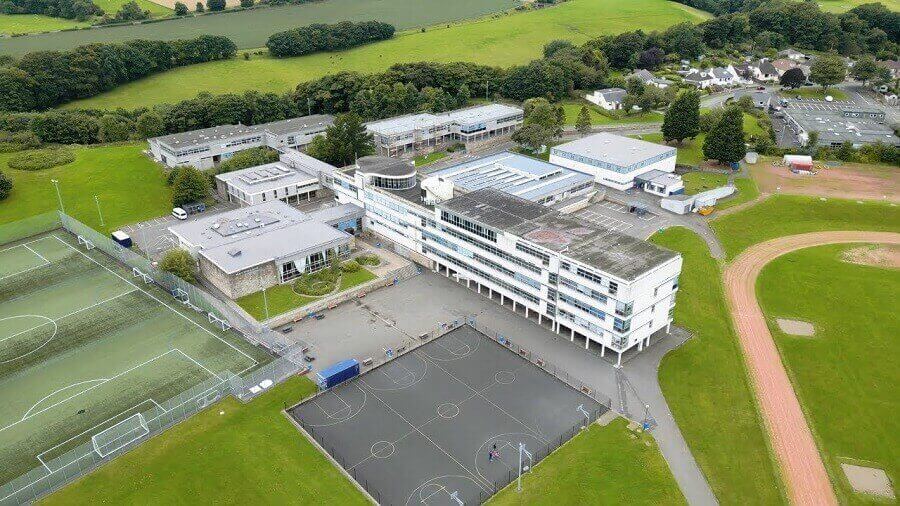 Aerial view of school campus with multiple buildings, sports pitches, and surrounding green fields