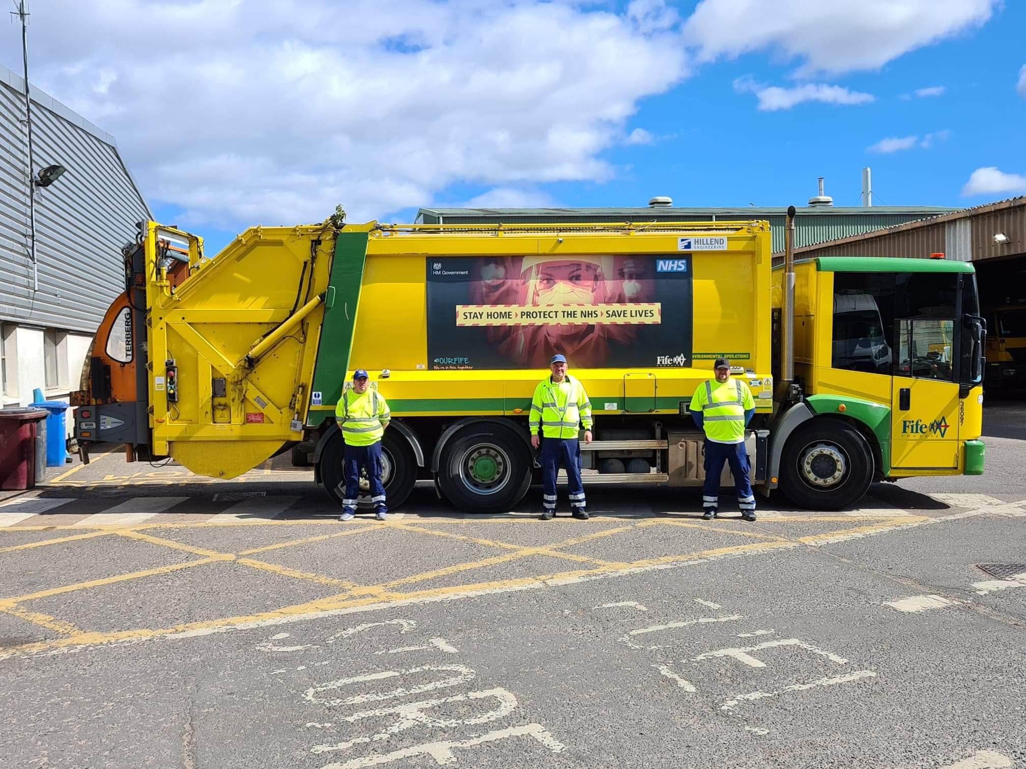 Three refuse workers standing in front of a Fife Council recycling truck with an NHS safety message on the side.