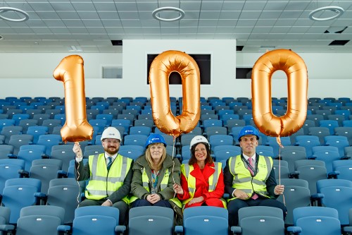 people sat in school assembly hall holding balloons saying 100 - One hundred days until the schools at Dunfermline Learning Campus open