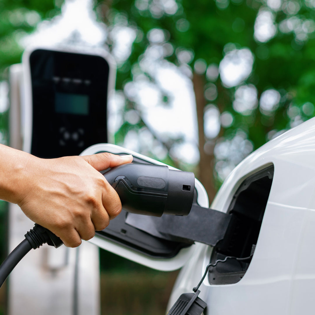 A hand holding an electric vehicle charger, pointed towards the charging point on an electric car - New EV Charging tariff set to support additional infrastructure in Fife