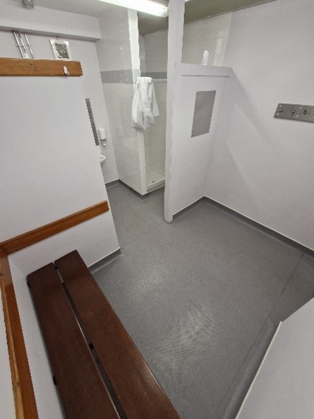 refs changing room A small changing room. Wooden benches line the wall. A shower stall is in back.
