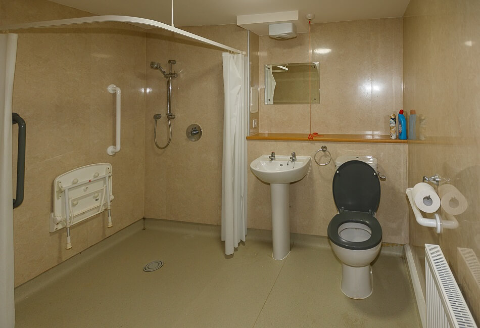 Image of an adapted bathroom, with wet floor, walk-in shower and toilet and basin