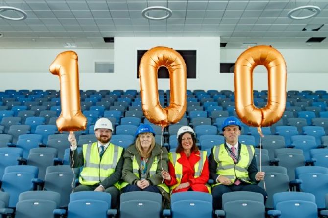people sat in school assembly hall holding balloons saying 100