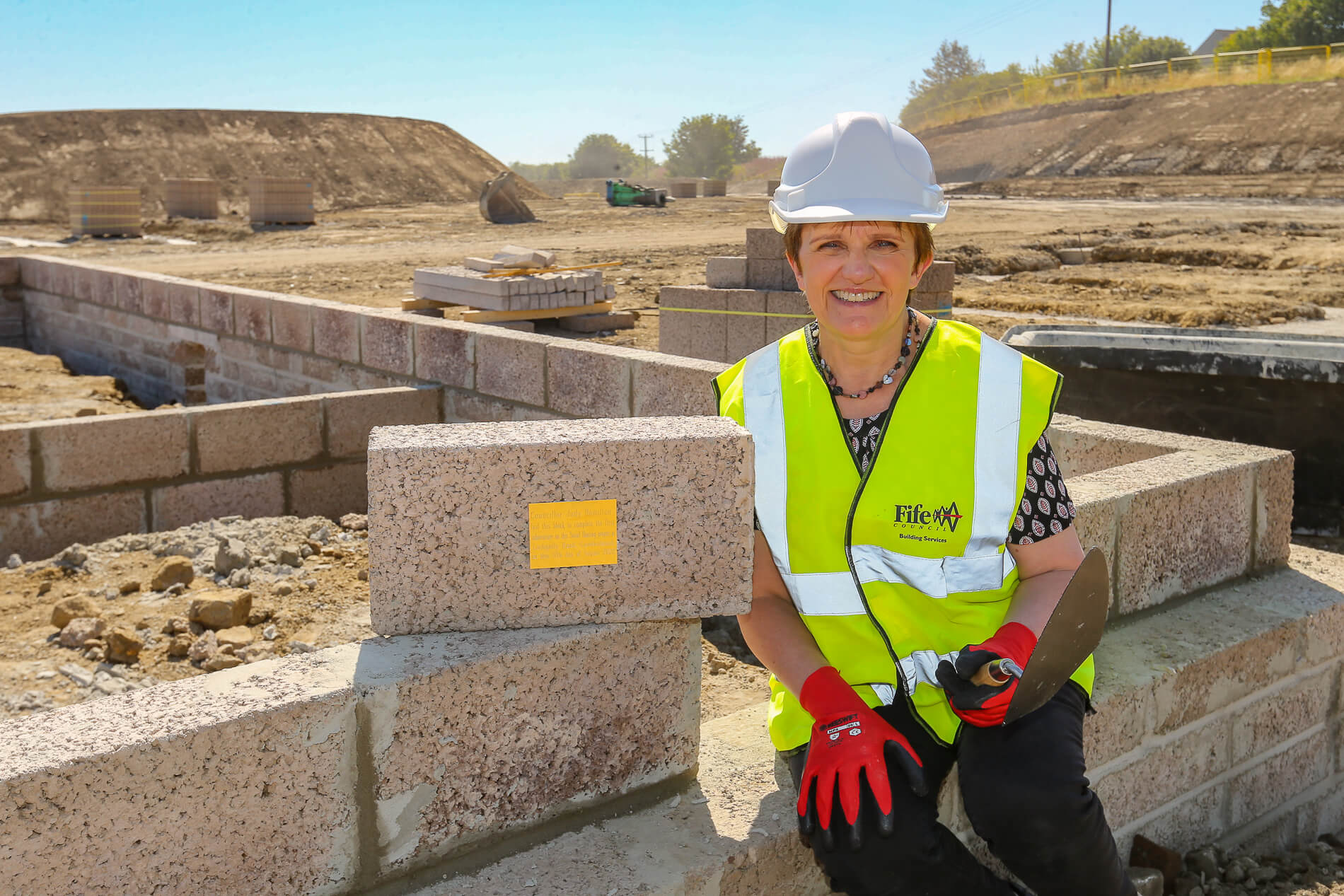 Cllr Judy Hamilton sitting on the wall of one of the new houses with the 'golden brick