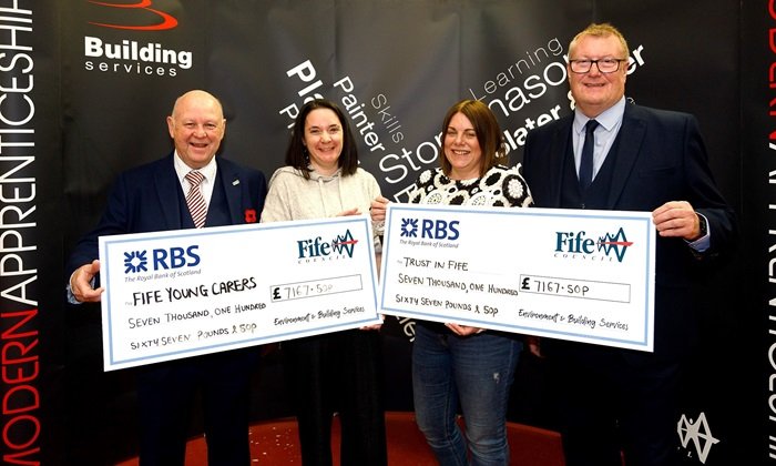 Presenting the cheques to the charities Four people stand holding oversized cheques, smiling to the camera. They are, left to right, Ross Grieve (Service Manager for Fife Council's Building Services), Jodie Burns (Fife Young Carers), Caroline McCall (Trust in Fife) and Neil MacGregor (Fife Council's Team Manager for Building Services).