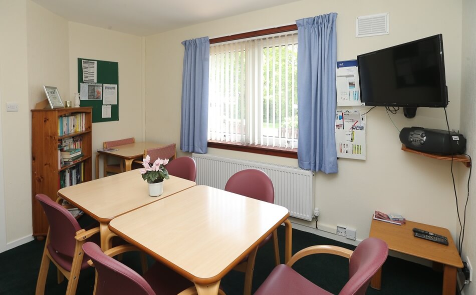 Communal living area at Elm Place, with table and chairs and bookcase