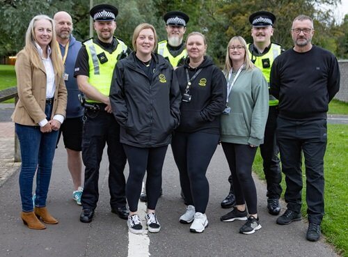 Funding secured for dedicated police officer tackling anti-social and violent crime in Glenrothes A group of nine people standing outdoors on a path, including several individuals wearing police uniforms and others in casual clothing, posing for a group photo