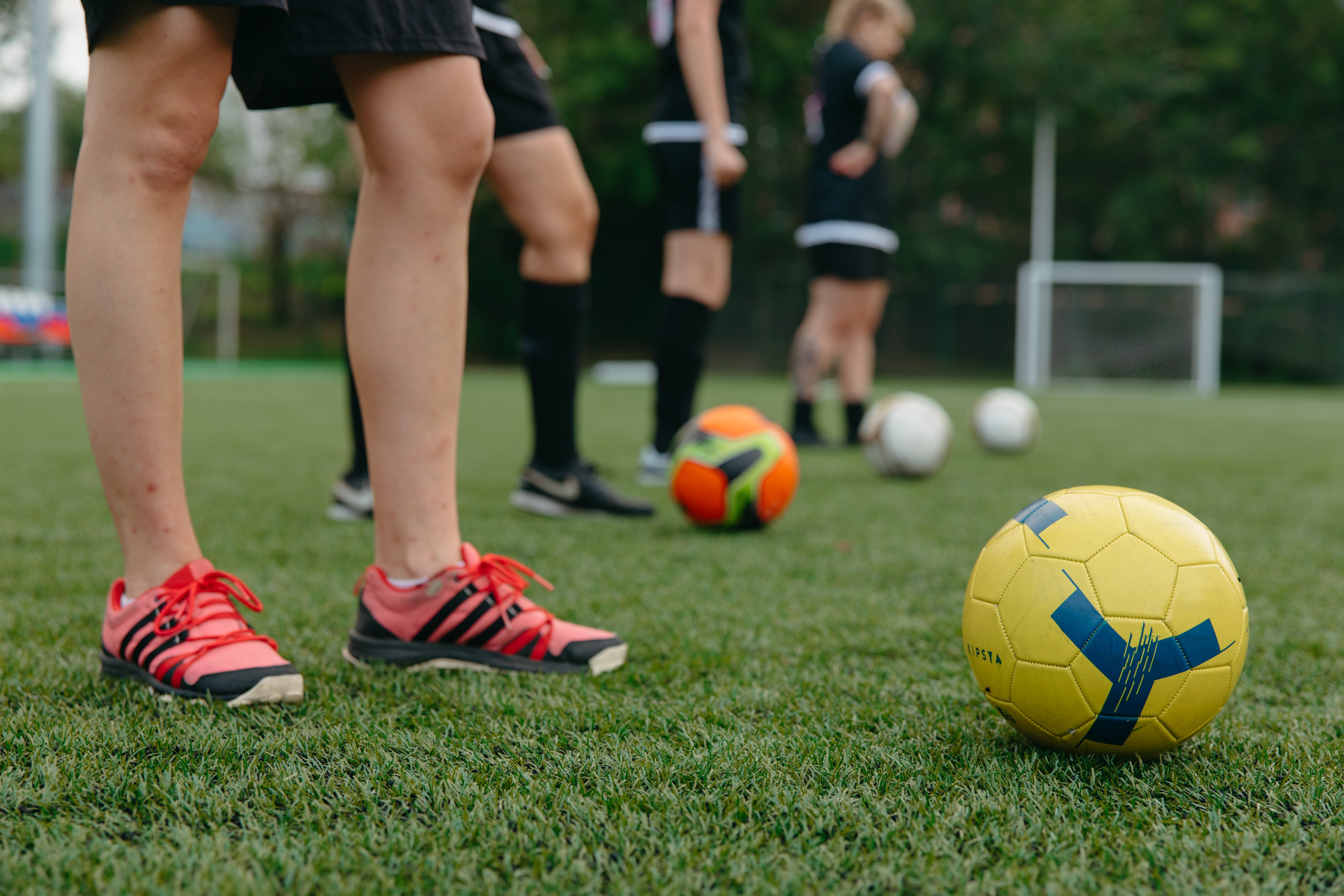 Abstract image of four people in front of footballs on a synthetic pitch.