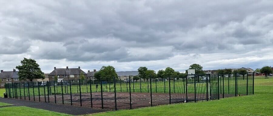 An outdoor fenced sports court. Green grass surrounds the court. An outdoor fenced sports court. Green grass surrounds the court.