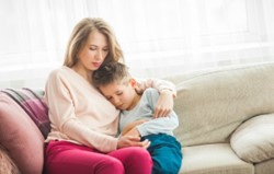 A woman and young boy sitting on a sofa, cuddling together as if upset