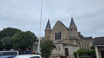 A stone building with two pointed turrets and a gabled roof, viewed from a parking area