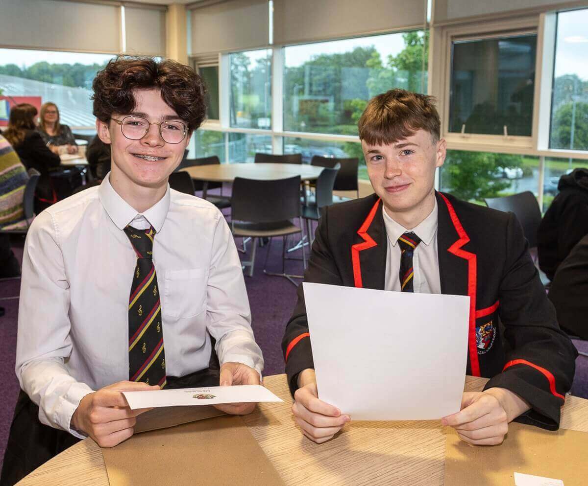 Two pupils look at the camera smiling holding their exam results paper in both hands