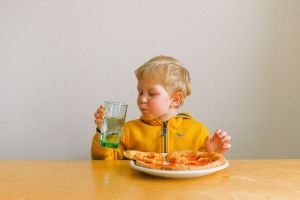 Little boy sitting at a table eating pizza and drinking water