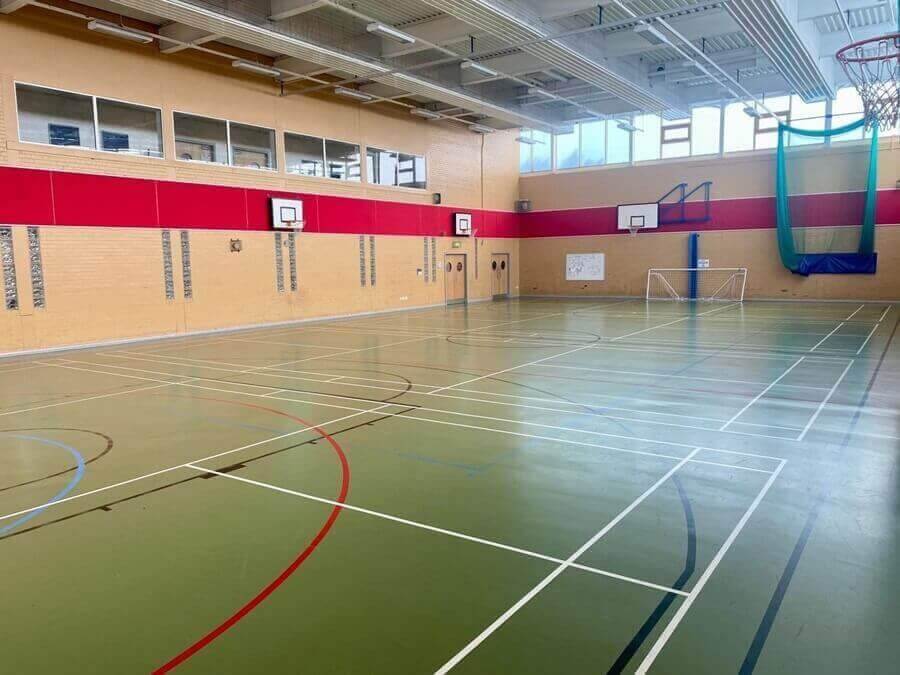Sports hall An empty indoor sports hall with marked courts, basketball hoops, high windows, and a small football goal against the far wall