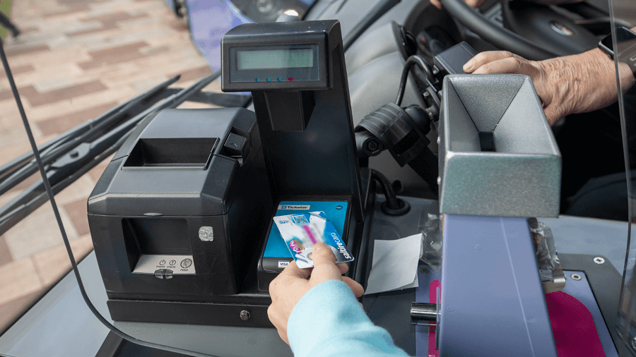 Close-up of a person scanning a bus pass card on a ticket machine inside a bus, with the driver visible in the background Close-up of a person scanning a bus pass card on a ticket machine inside a bus, with the driver visible in the background